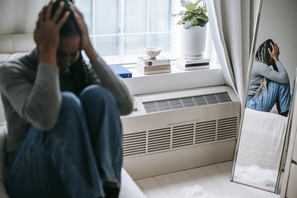 Frustrated mom is having strong emotions and feeling burned out. This North Carolina Mom is sitting alone with her image being reflected in a mirror.