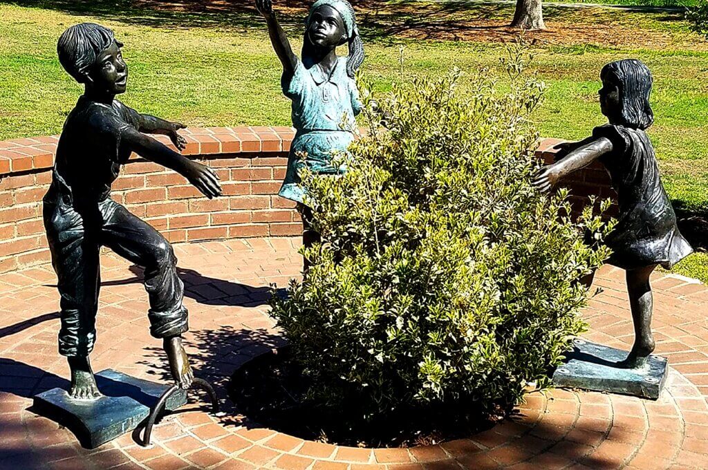 Mindfulness Walk | Brainspotting Therapist | Brainspotting Charlotte | Rock Hill, SC | 28277 | 29708 | 28036 | Open field bathed in sunlight, statues of children playing, with benches for mindful rest, ideal after Brainspotting Therapy reflection in Rock Hill, SC.