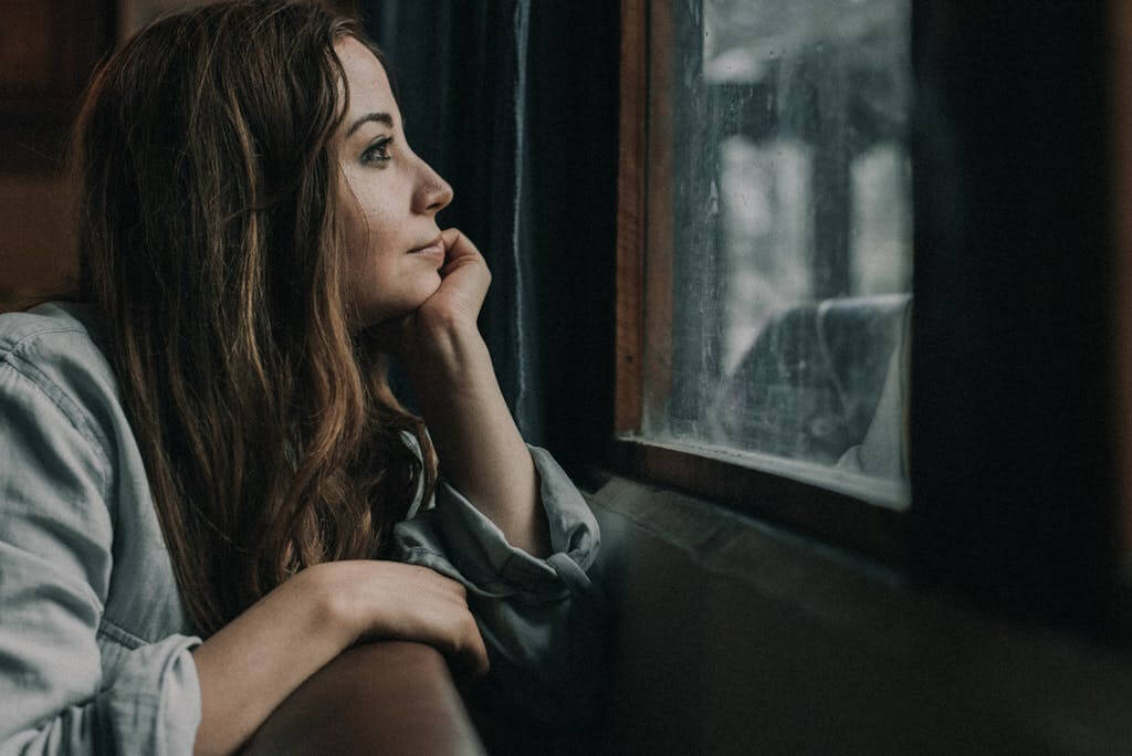 Overwhelmed mom in Asheville NC considering online therapy and Brainspotting therapy Woman sitting quietly at home in Asheville, NC, looking thoughtful before beginning online therapy with Mosaic Reflections | Therapy for Anxiety | Trauma Counseling | Brainspotting Therapy