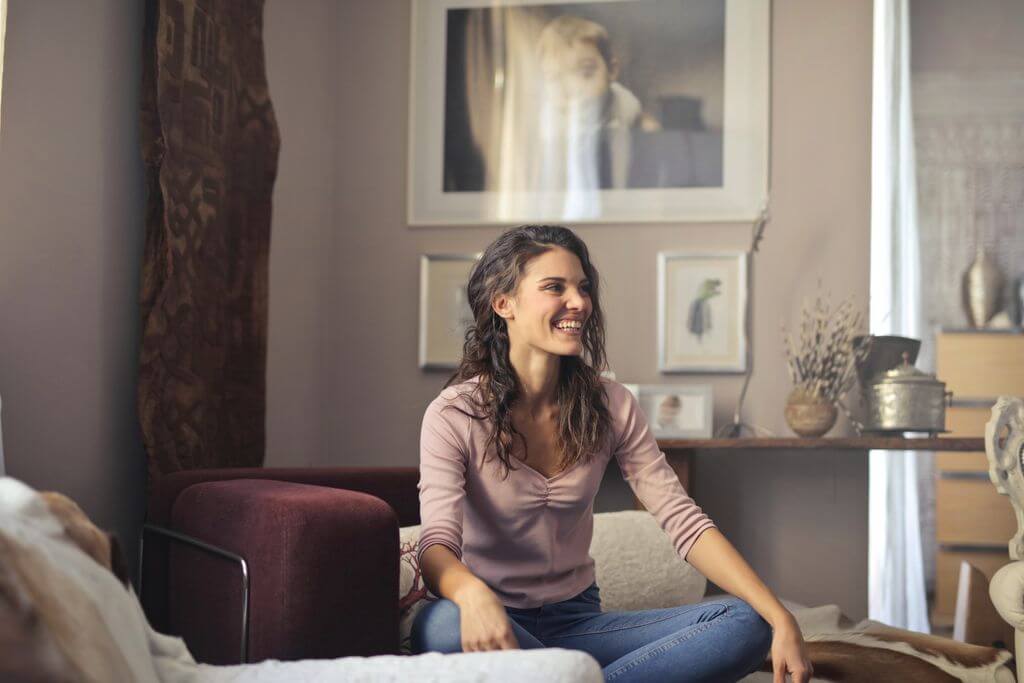 A relaxed woman smiling while sitting in a stylish, cozy living room.